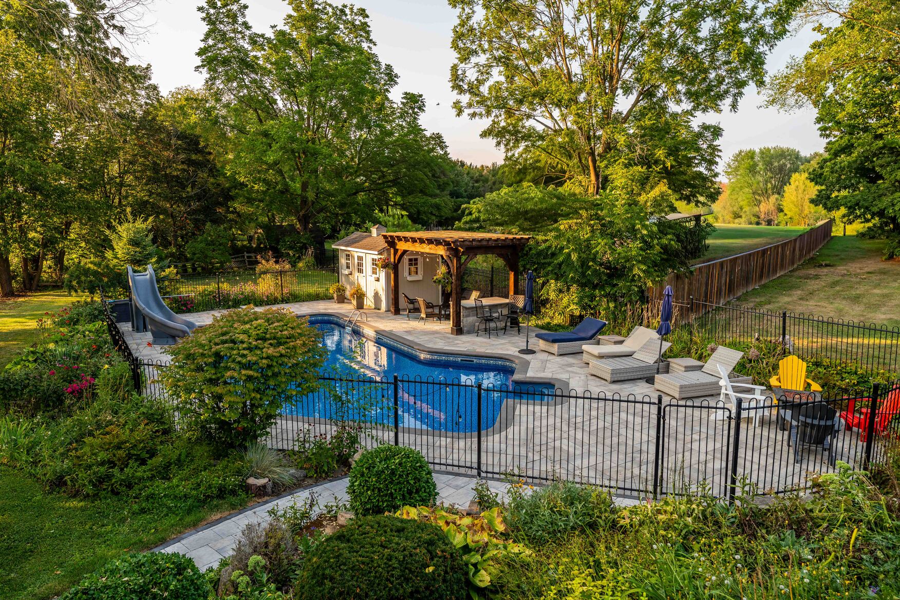Pool with hardscape patio, pergola, and wrought iron fencing
